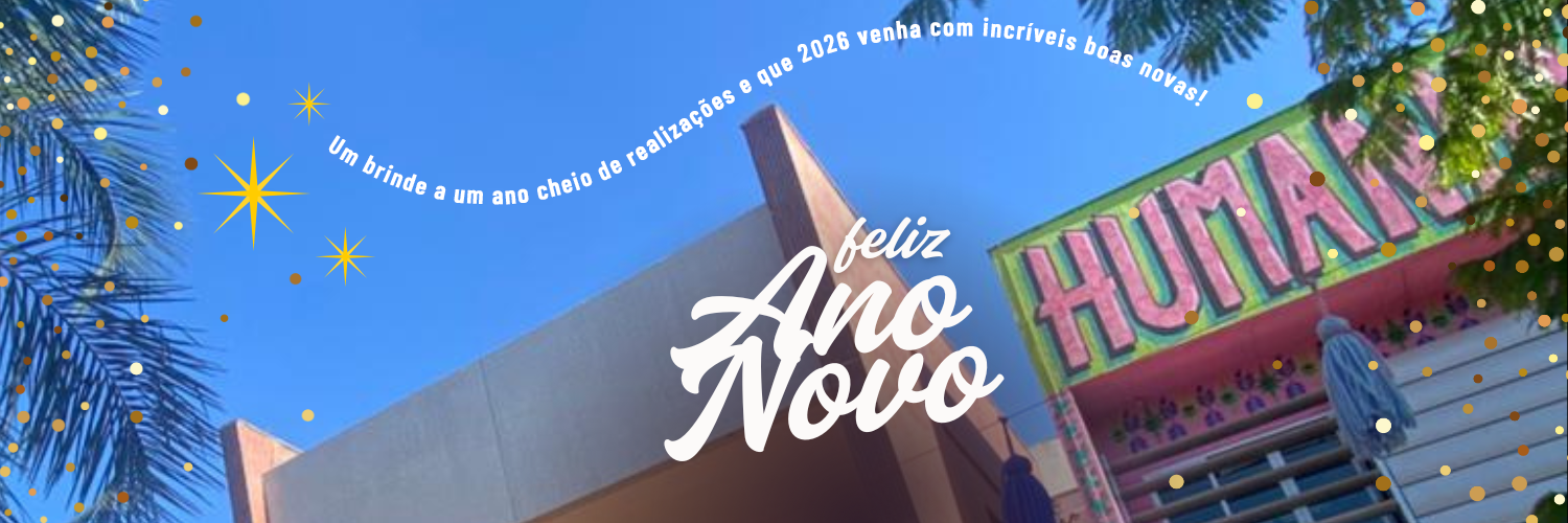 foto do prédio da FCS vista de baixo para cima, com um céu azul e coqueiros. Na imagem estã escrito feliz ano ano de branco, e um texto em fonte pequena  num formato de cauda de estrela cadente:      Um brinde a um ano cheio de realizações e que 2026 venha cheio de boas novas! 