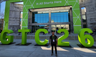 Um homem posa sorridente em frente ao San Jose McEnery Convention Center, onde se lê "NVIDIA GTC" e a frase "It All Starts Here" em um grande painel verde. À sua frente, destacam-se grandes letras e números verdes que formam a sigla "GTC 26". O cenário externo é amplo e moderno, sob a luz do dia, indicando a participação em um evento tecnológico de grande porte.