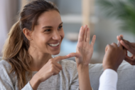 Imagem mostra mulher em comunicação com outra pessoa por meio de linguagem de sinais. 