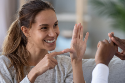 Imagem mostra mulher em comunicação com outra pessoa por meio de linguagem de sinais. 