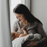 Imagem mostra mulher amamentando seu bebê por trás de uma cortina