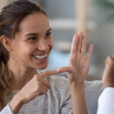 Imagem mostra mulher em comunicação com outra pessoa por meio de linguagem de sinais. 