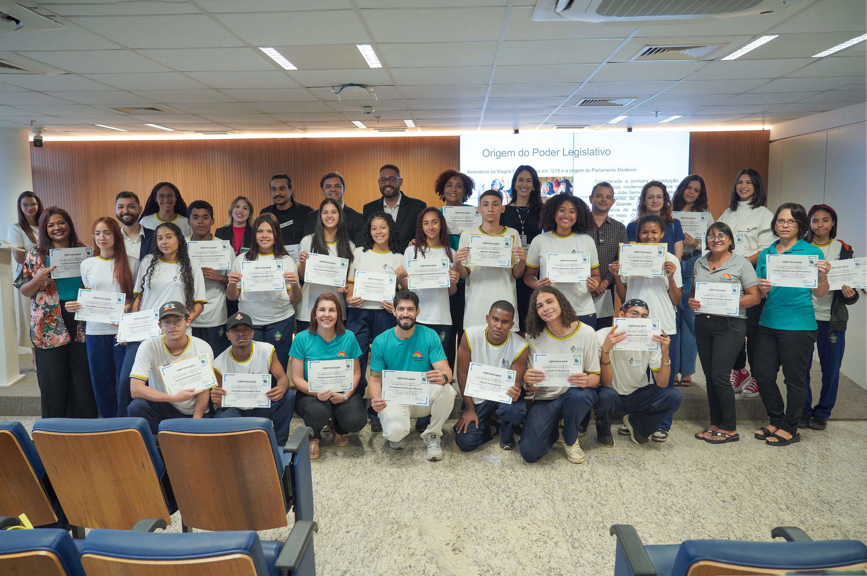 Participantes da homenagem na Assembleia Legislativa. Na foto: várias pessoas, adultos e jovens, reunidos, posam para a foto com os certificados na mão. 