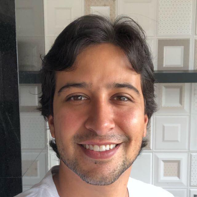 Foto do Caio Almeida do Amaral. Homem jovem, pardo, cabelos e barba pretos, sorrindo.