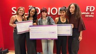#ParaTodosVerem Foto em grupo de todas as cinco vencedoras posando juntas na frente da parede vermelha com o letreiro do Salão Nobre. Elas seguram seus respectivos cheques simbólicos. As duas de vestido preto seguram o cheque do 3º lugar (esquerda); a jovem de cabelo ruivo o do 1º lugar (centro); e as duas de jaqueta e blusa marrom o do 2º lugar (direita). Todas sorriem para a câmera.