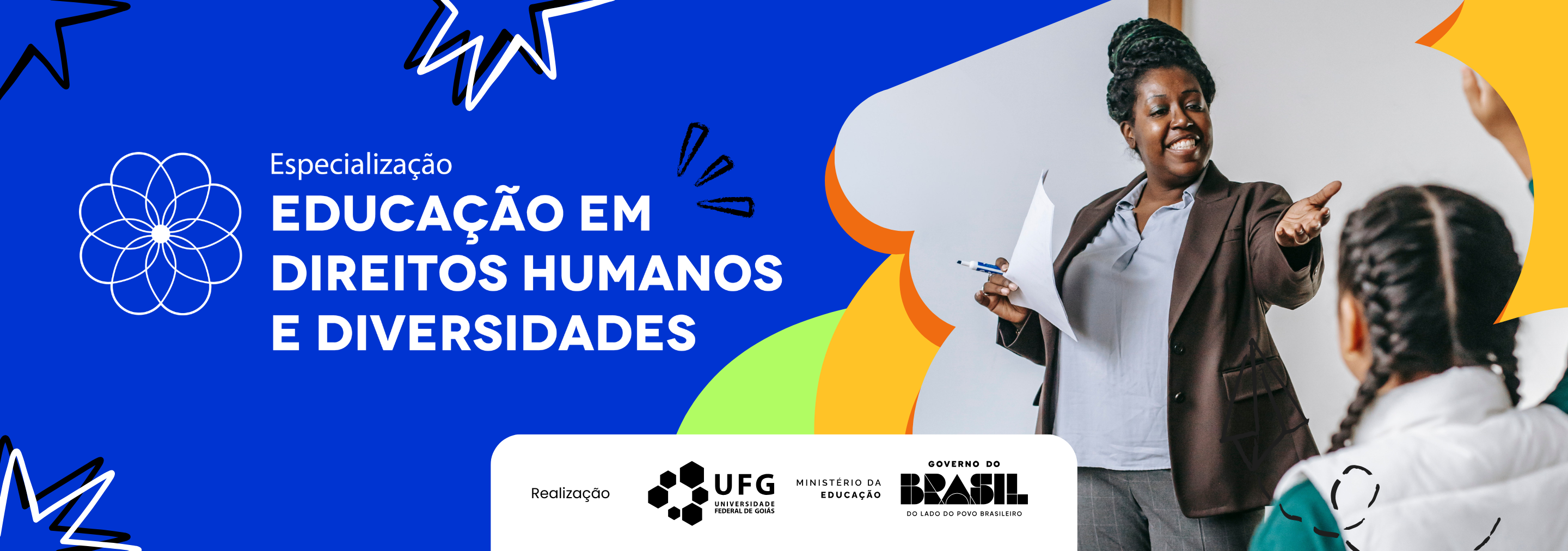 Banner com imagem em formato horizontal, com fundo azul. Trata-se do anúncio de um curso de Especialização em Direitos Humanos e Diversidades. Centralizado, sobre fundo azul, está o texto em letras brancas: Especialização: Educação em Direitos Humanos e Diversidades. Ao lado, há um símbolo geométrico branco semelhante a uma flor. No lado direito da imagem, há a fotografia de uma mulher negra, adulta, com cabelo crespo enrolado em um coque, sorrindo e apontando para uma estudante. A mulher está enquadrada da cintura para cima e veste blusa clara e blazer marrom. Na sua frente, aparece as costas desfocadas de uma estudante negra, com cabelos negros e trançados, blusa verde e colete cinza, levantando a mão. Na parte inferior, sobre fundo branco, estão os logotipos das instituições de apoio: CIAR, NDH, UFG, Ministério da Educação e Governo do Brasil.