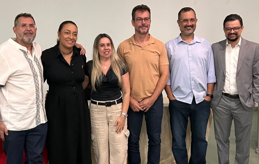 Programas de Pós-Graduação Interdisciplinares da UFG#ParaTodosVerem:Seis pessoas sorridentes posam lado a lado contra um fundo claro. Da esquerda para a direita: um homem de bata branca e óculos; uma mulher de vestido longo preto; uma mulher loira de blusa preta e calça bege; um homem de polo bege; um homem de camisa social azul-clara; e um homem de fato cinzento e óculos.