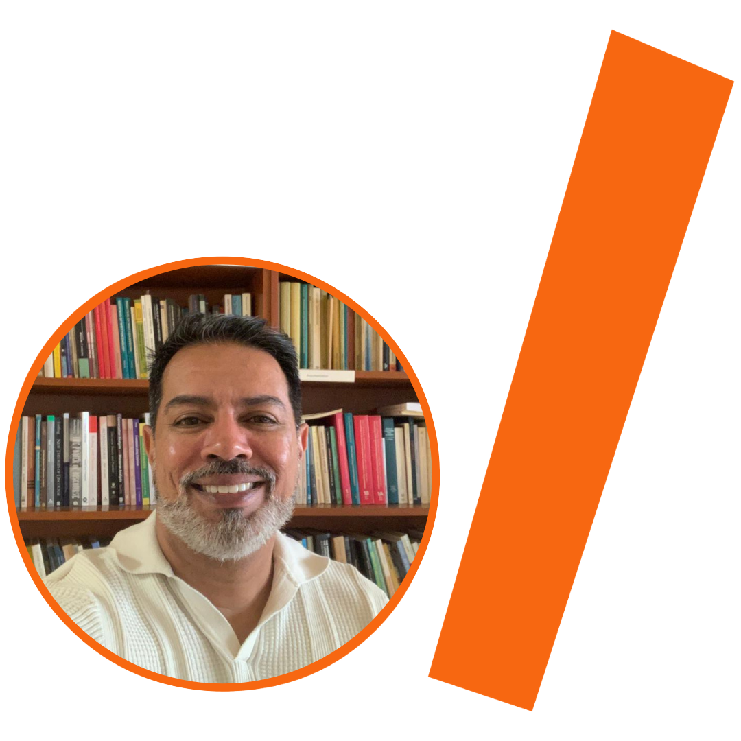 Imagem com fundo bege e elementos gráficos em laranja. À esquerda, dentro de uma moldura circular com borda grossa laranja, há a foto de um homem sorrindo para a câmera. Ele tem pele parda, cabelos escuros e curtos, com barba e bigode grisalhos, e veste uma camisa branca com gola. Ao fundo de sua foto, vê-se uma estante de madeira repleta de livros coloridos. À direita da imagem, uma larga faixa retangular e sólida, também na cor laranja, cruza o espaço na diagonal, lembrando uma barra inclinada.