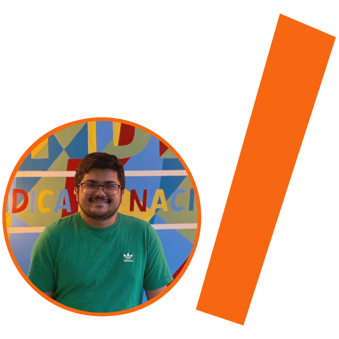 #ParaTodosVerem: Imagem com fundo bege. À esquerda, dentro de uma moldura circular laranja, há a foto de um homem jovem de pele clara, cabelos e barba escuros e curtos, usando óculos de grau e camiseta verde com a logo da Adidas. Ele sorri. Atrás dele, vê-se um painel colorido com formas geométricas e letras que formam partes das palavras "DICA" e "NACI". À direita da imagem, há uma larga faixa diagonal retangular, também na cor laranja.
