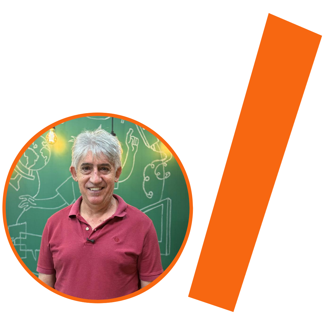 #ParaTodosVerem: Fotografia colorida em plano médio de um homem branco de meia-idade, com cabelos grisalhos curtos e um sorriso largo. Ele veste uma camisa polo na cor rosa antigo e olha para a câmera. Ele está inserido em um recorte circular com borda laranja. Ao fundo, uma parede verde (estilo lousa) com desenhos e esquemas em giz branco e a luz de uma lâmpada de filamento. À direita do círculo, há uma barra grossa e inclinada também na cor laranja. O conjunto visual, segue a identidade visual do projeto.