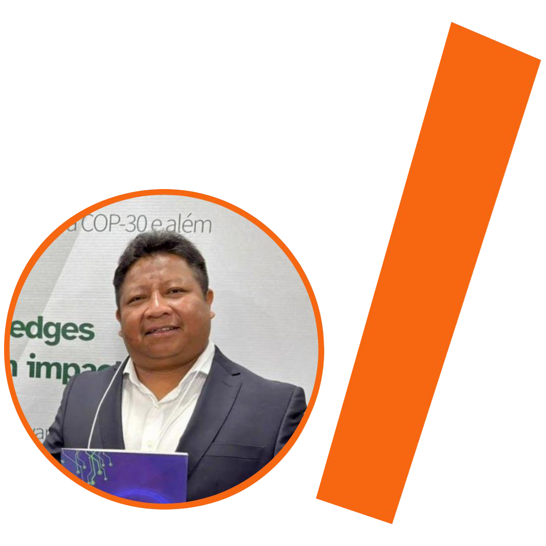 #ParaTodosVerem: Fotografia colorida em plano médio de um homem indígena sorrindo. Ele tem cabelos pretos curtos e veste um paletó azul-marinho sobre uma camisa social branca. Na parte inferior do recorte, ele segura uma brochura ou pasta azul. A imagem está inserida em um recorte circular com borda laranja. Ao fundo da foto, vê-se parte de um banner de evento na cor branca com textos em verde e cinza, onde se lê a inscrição "COP-30 e além". À direita do círculo, há uma barra grossa e inclinada na cor laranja. O conjunto visual está mantendo a identidade visual padrão do projeto.