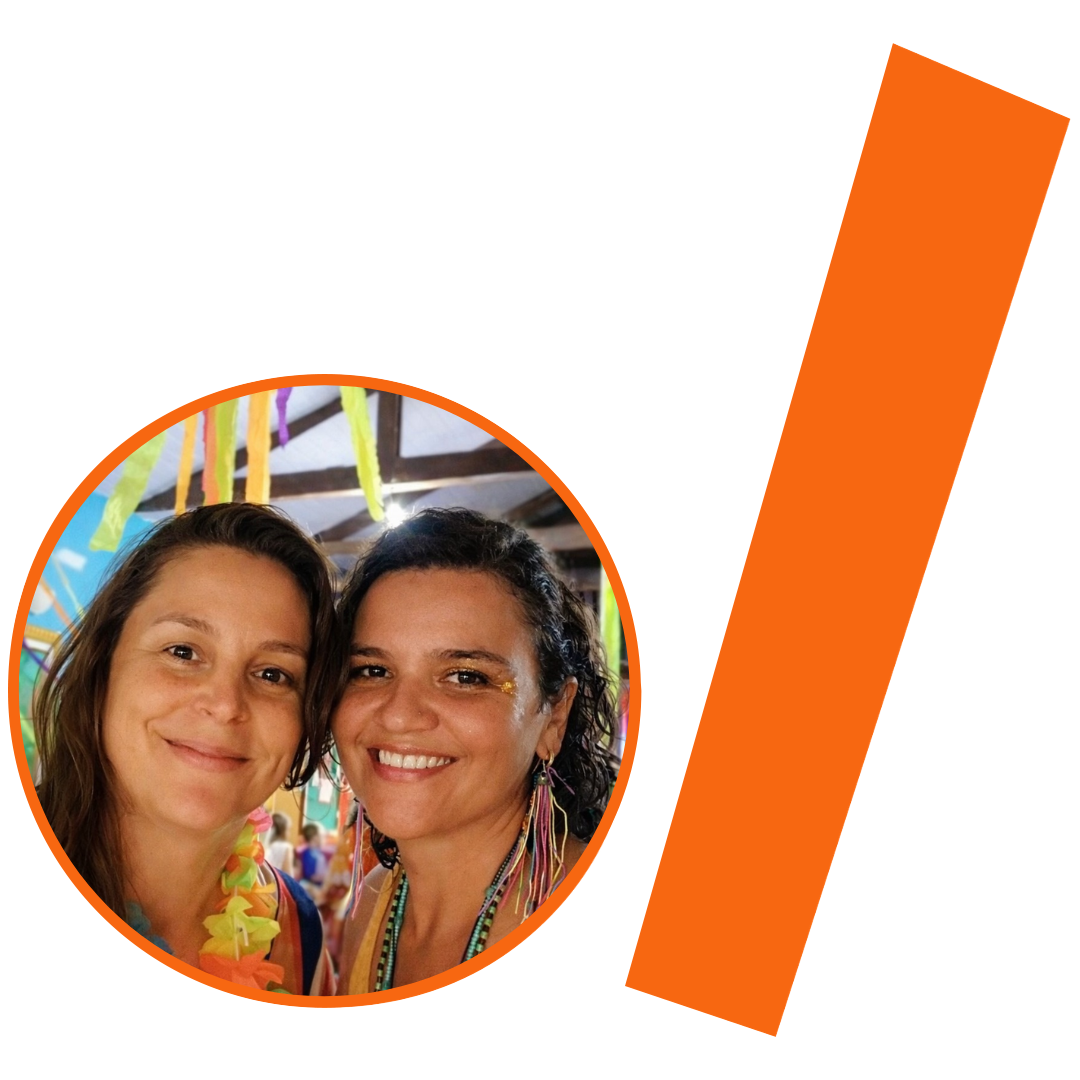 #ParaTodosVerem: Fotografia colorida em plano médio de duas mulheres brancas, sorrindo e com os rostos próximos, posando para a câmera. Ambas usam maquiagem com glitter nos olhos e colares coloridos. A mulher à esquerda tem cabelos castanhos claros e lisos; a da direita tem cabelos pretos e cacheados, além de brincos grandes de franjas coloridas. A imagem está inserida em um recorte circular com borda laranja. Ao fundo da foto, vê-se um ambiente de festa junina, com bandeirinhas coloridas penduradas e teto de madeira desfocados. À direita do círculo, há uma barra grossa e inclinada também na cor laranja. O conjunto visual mantém a identidade visual padrão do projeto.