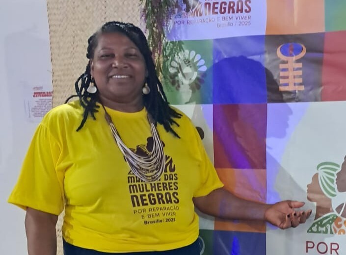 Uma mulher negra, com tranças, camiseta amarela e em um fundo colorido