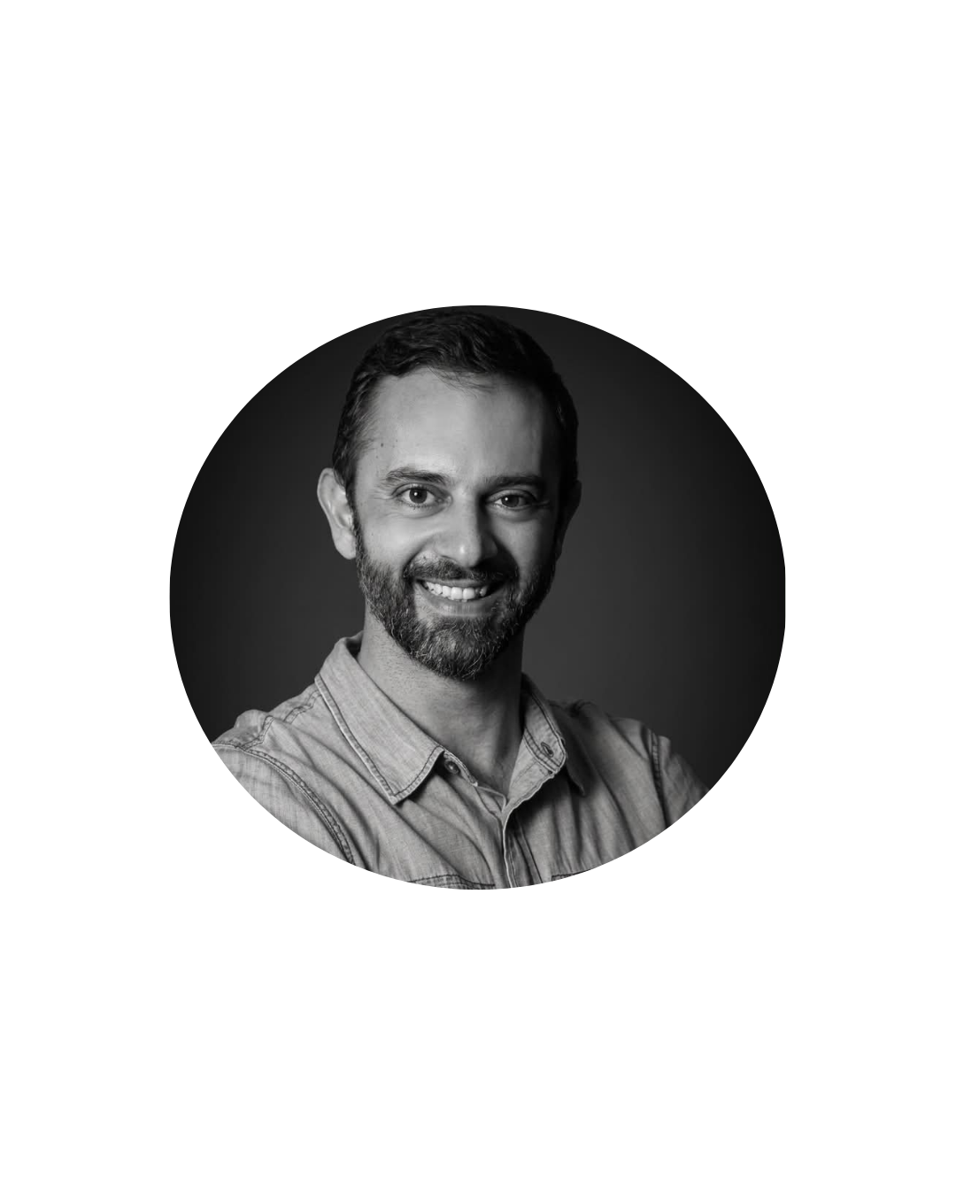 Retrato em preto e branco de um homem sorrindo dentro de um recorte circular. Ele tem barba curta, usa camisa clara de botões e aparece com os braços cruzados. O fundo interno do retrato é escuro e neutro, destacando o rosto da pessoa.