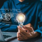 Imagem mostra homem segurando lâmpada enquanto utiliza computador